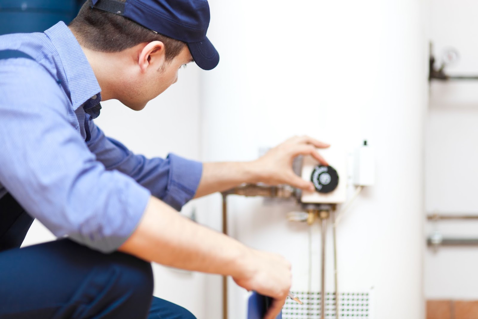 A man in blue overalls repairs a water heater, ensuring its proper functioning and preventing potential issues.