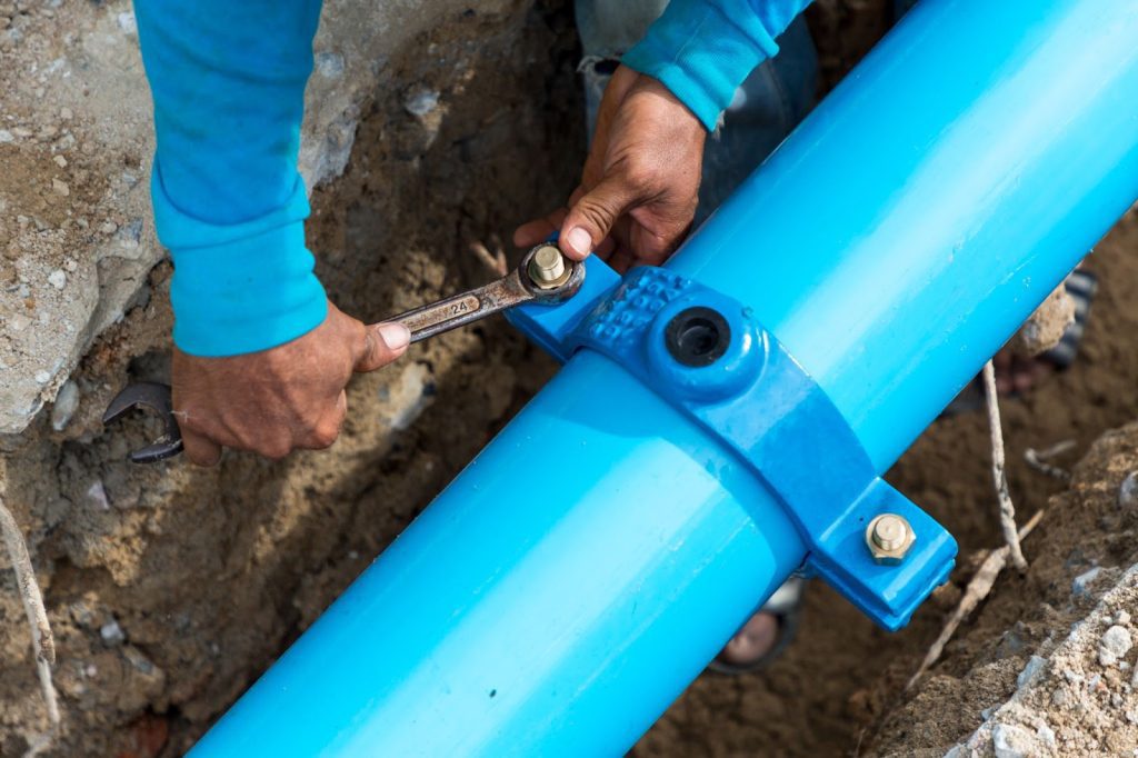 A professional plumber fixing a blue pipe with a wrench - water main maintenance.