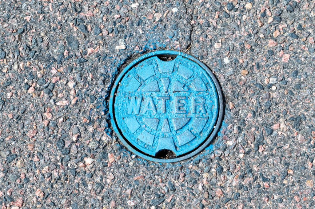 A blue manhole cover labeled Water indicating a broken water main, highlighting the need for professional plumbing services.