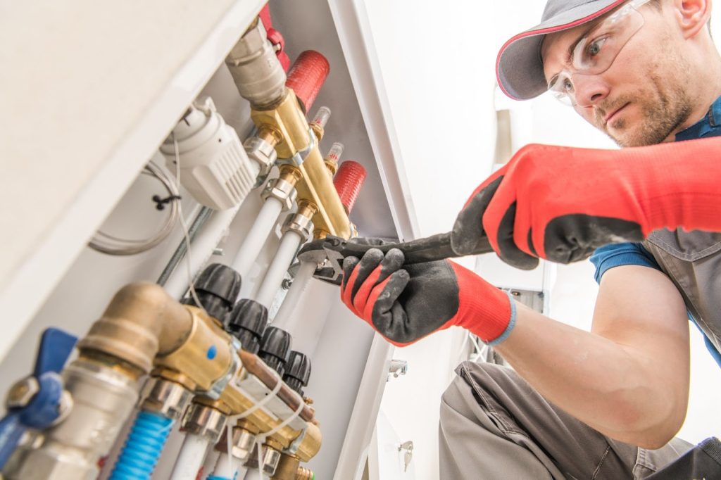 A man in a red hat and gloves fixing a water heater. Secure plumbing, plumbing maintenance, plumbing system.