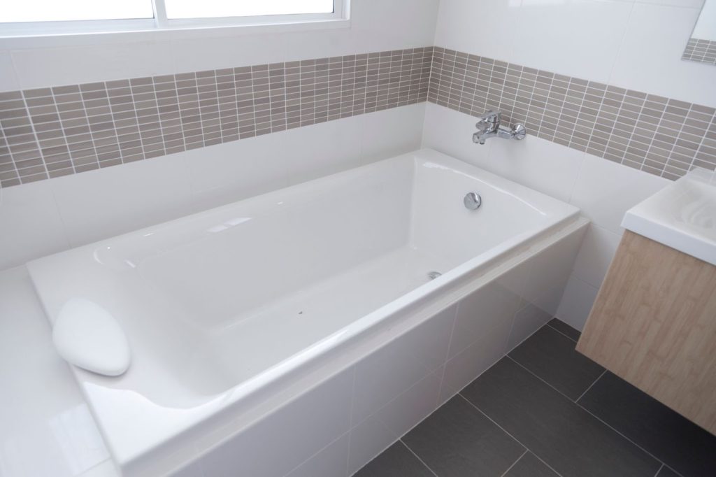 A white bathtub in a bathroom, part of a bathtub project, installed by a professional plumber.