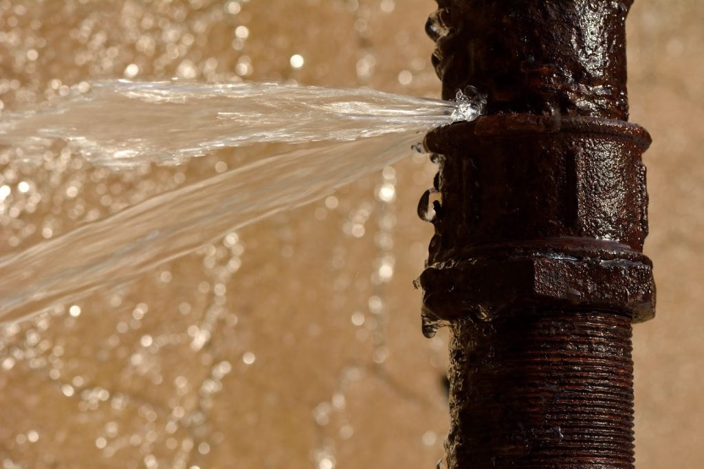 Close-up of burst water pipe with water gushing out, causing water damage.