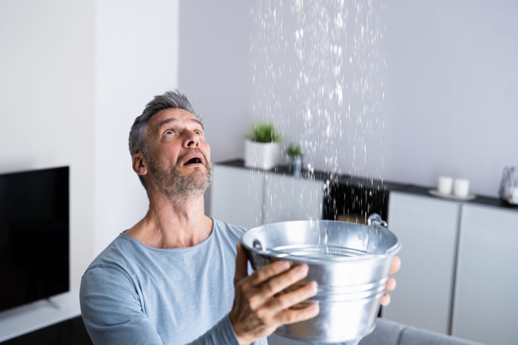 Man pouring water from bucket into bucket. Burst pipes causing water damage.