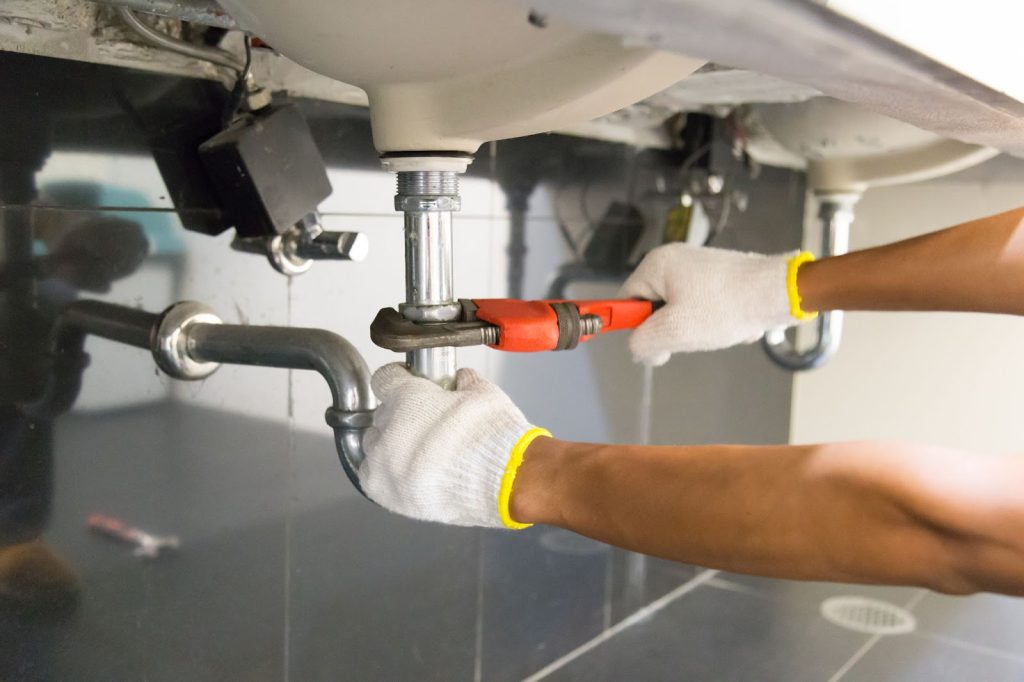 Person in white shirt and gloves fixing sink. Secure plumbing, maintenance, plumbing system.