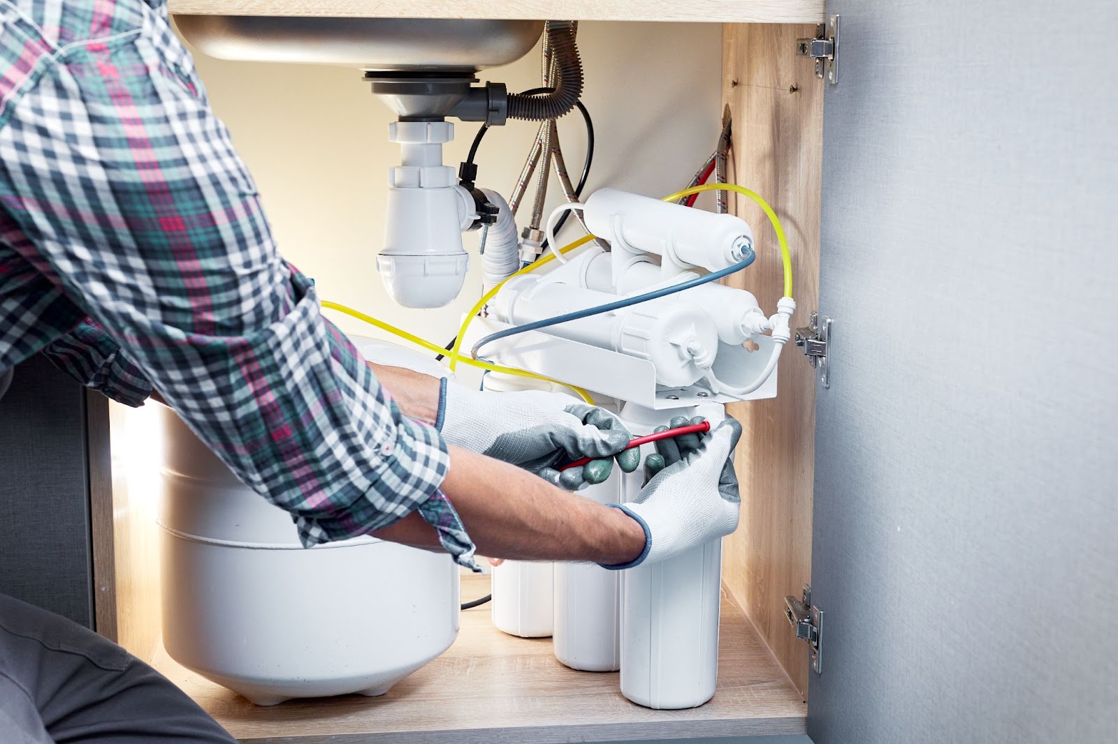 A man repairs a water filter in a modern kitchen, focusing intently on the task at hand