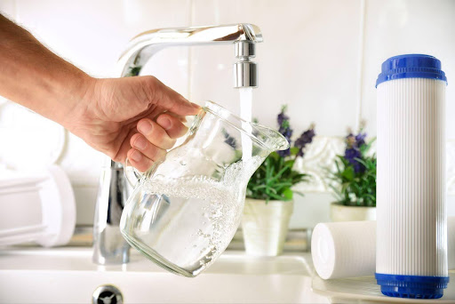 A person holds a clear glass filled with water, freshly poured from a kitchen faucet