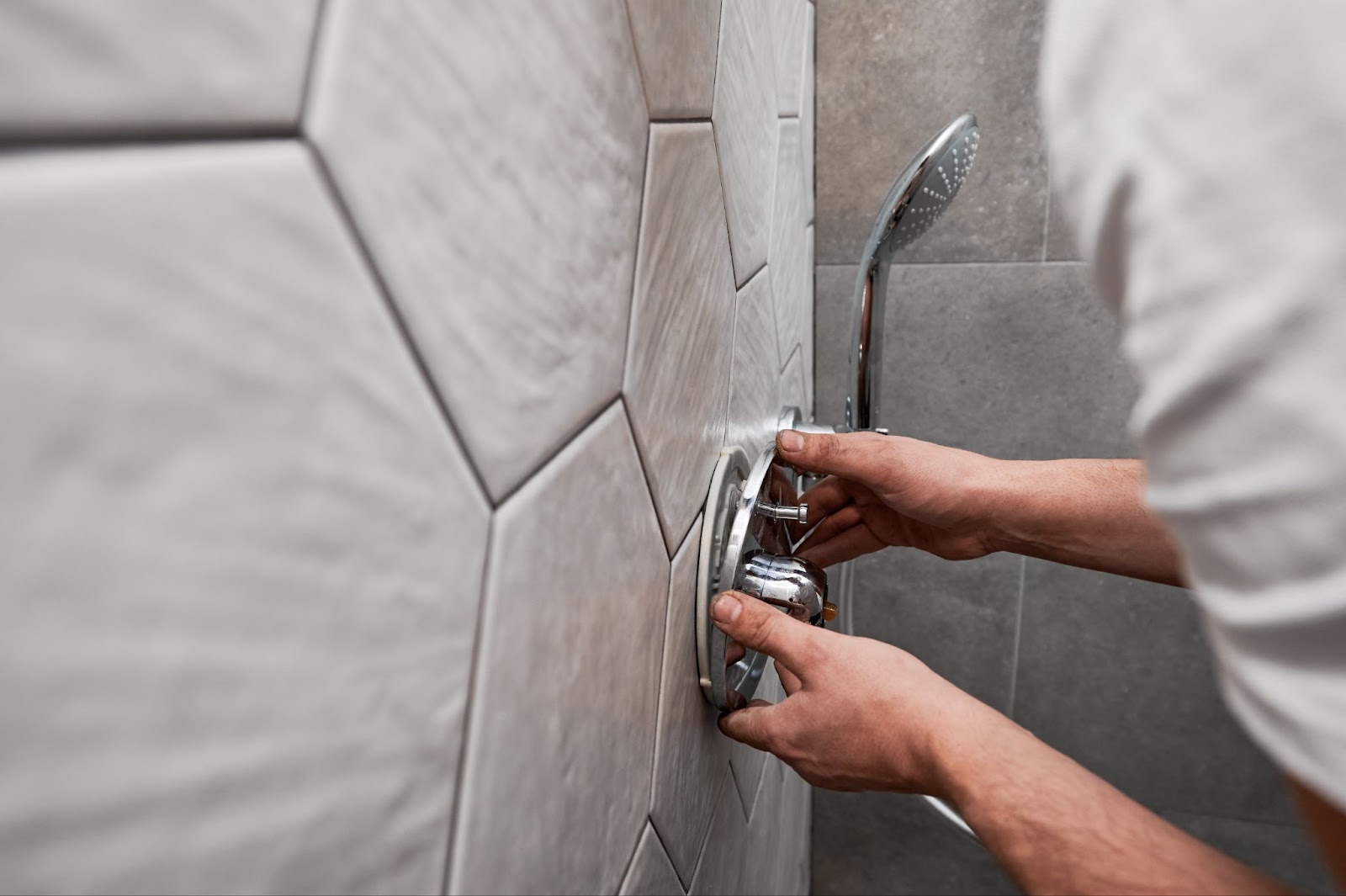 A plumber repairs a shower head on a wall, ensuring proper installation for optimal water flow in the bathroom.