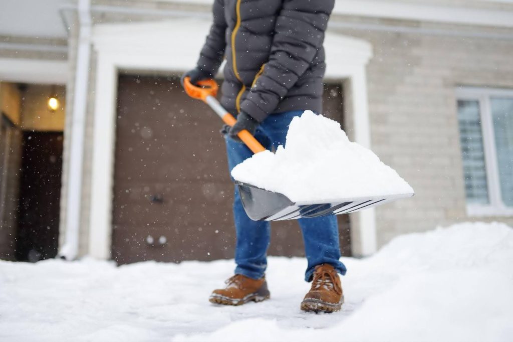 A man shoveling snow from the sidewalk for pedestrian safety in winter