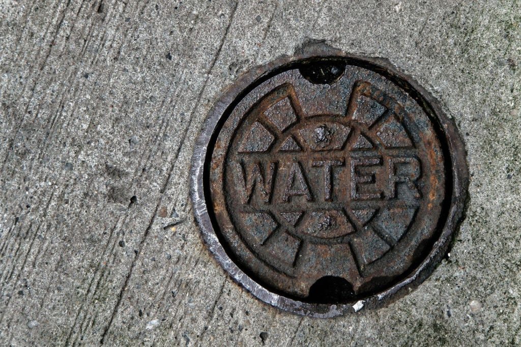 A manhole cover featuring a prominent water symbol, set against a concrete surface