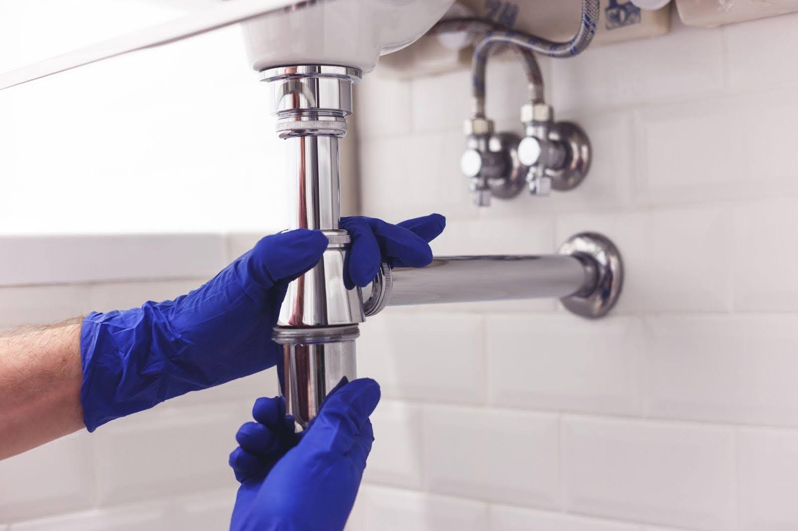 An individual in blue gloves is engaged in fixing a sink, showcasing hands-on maintenance work