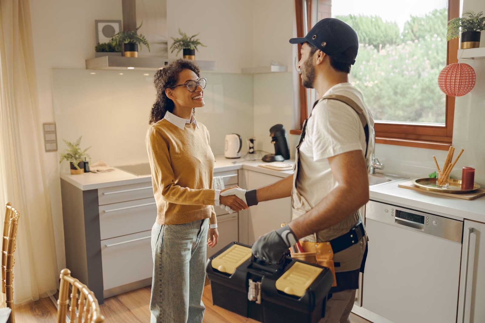 A man and woman shake hands in a kitchen, discussing plumbing repairs for an apartment.