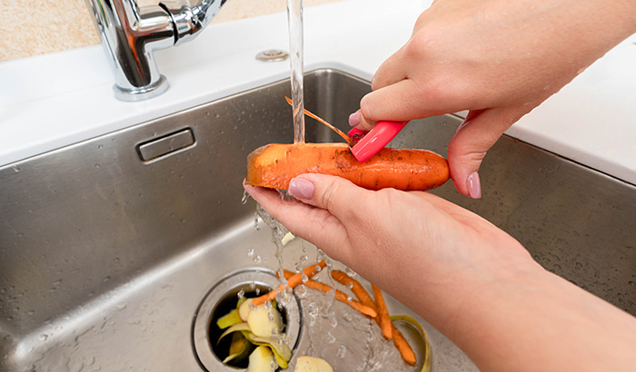 A person rinsing food by pouring water into a sink